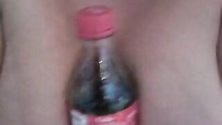 Naked girl holds a coke bottle in her boobs