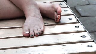 Women's dirty feet on a park bench.