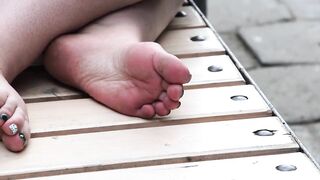 Women's dirty feet on a park bench.